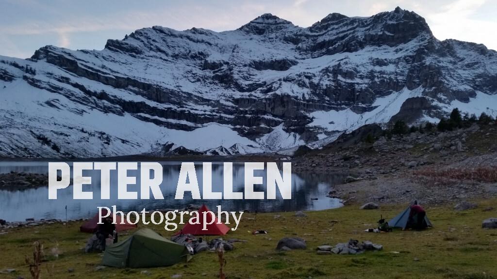 Four tents camping beside a lake at the foot of mountains in the Swiss Alps